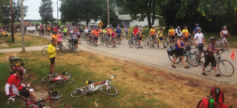 Thousands of RAGBRAI riders swarm a town square for a rest-and-refresh break, in Minburn, Iowa.