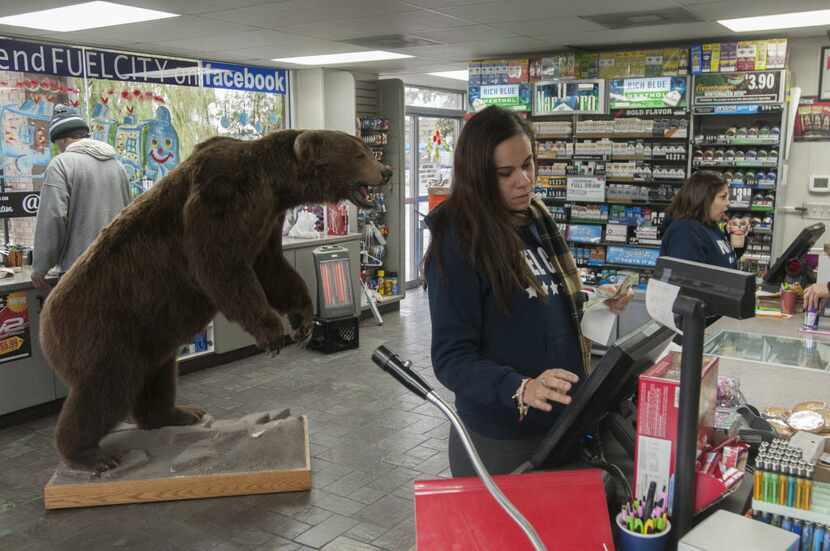 Blanca Ponce checks out customers at Fuel City.  Behind her is a stuffed brown bear, one of...