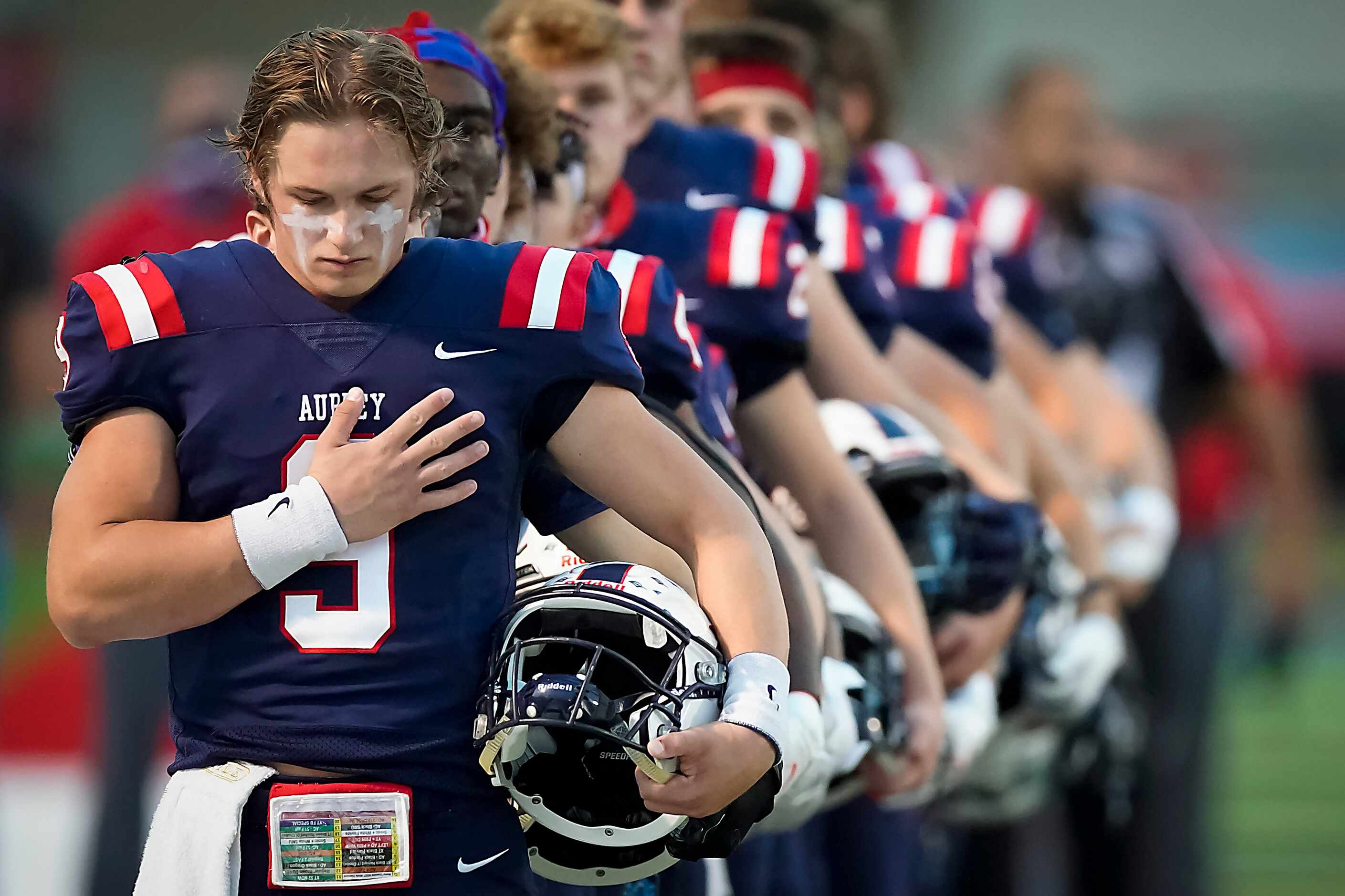 Aubrey quarterback Jaxon Holder stands for the national anthem with teammates before facing...