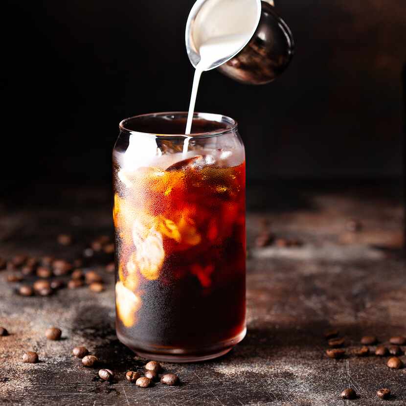 Cold brew iced coffee in a glass with milk or creamer pouring over