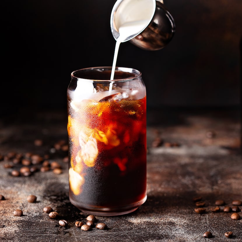 Cold brew iced coffee in a glass with milk or creamer pouring over