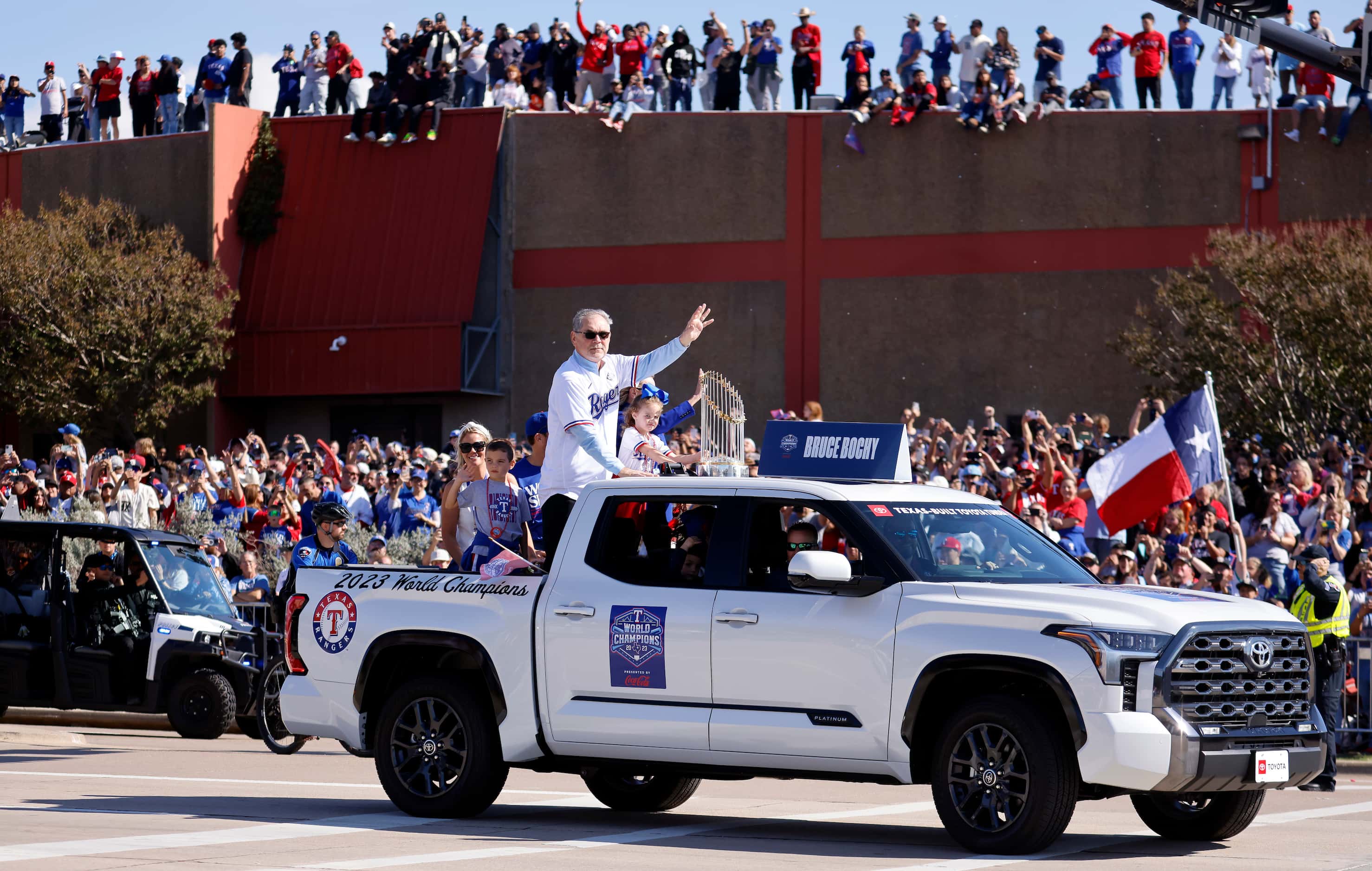 Riding with the Commissioner's Trophy, Texas Rangers manager Bruce Bochy waves to fans...