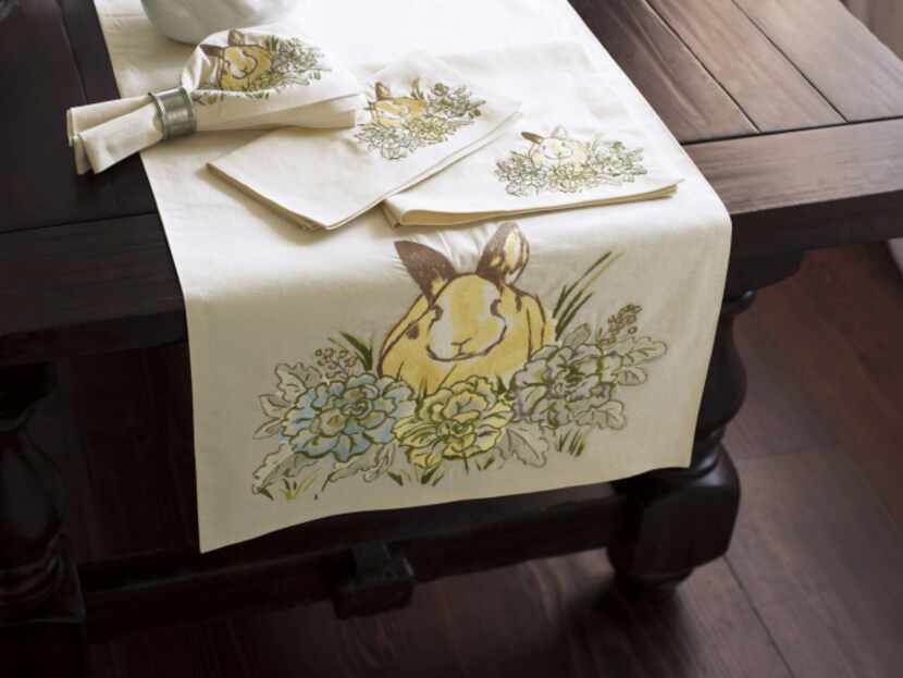 A crisp linen and cotton table runner is embroidered with a fanciful yellow bunny among...
