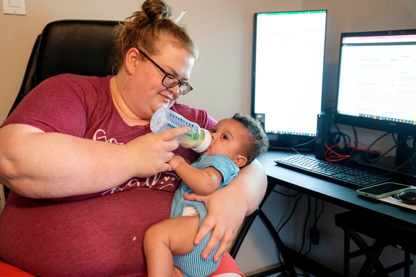 Eden Lovelady feeds her 6-month-old son Lucas Mbumwae while sitting at her home workstation....