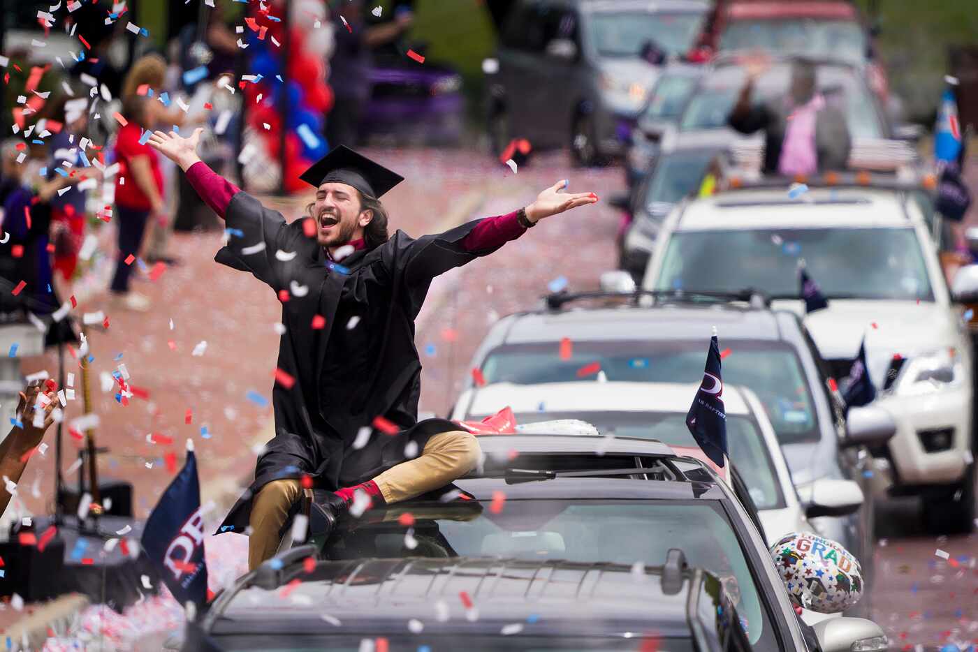 Graduate William Santini celebrates as confetti falls during a commencement car parade at...