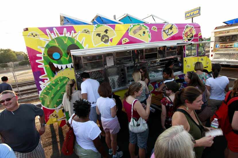 People snack on food from the 3 Men and a Taco truck during the Dallas Food Truck Festival....