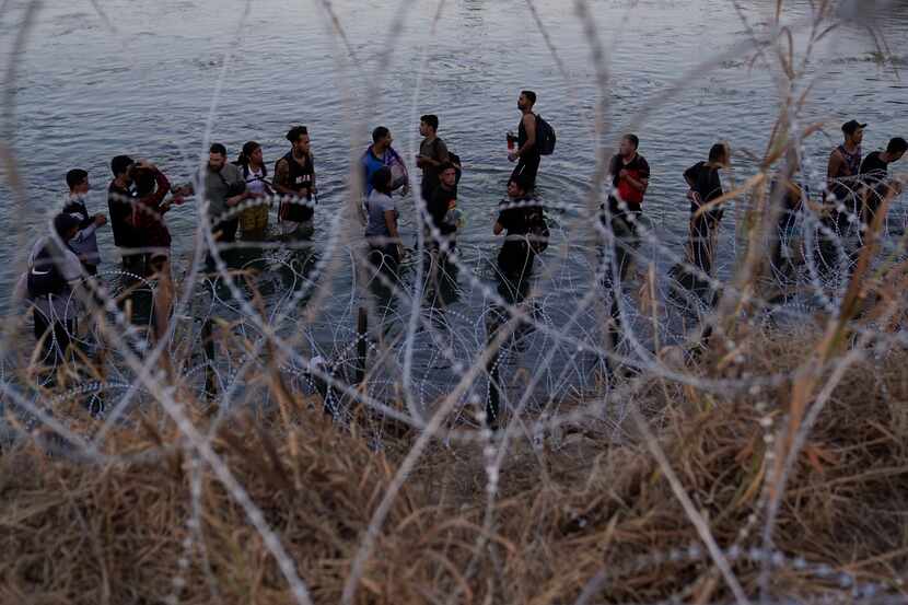 Migrants wait to climb over concertina wire after they crossed the Rio Grande and entered...