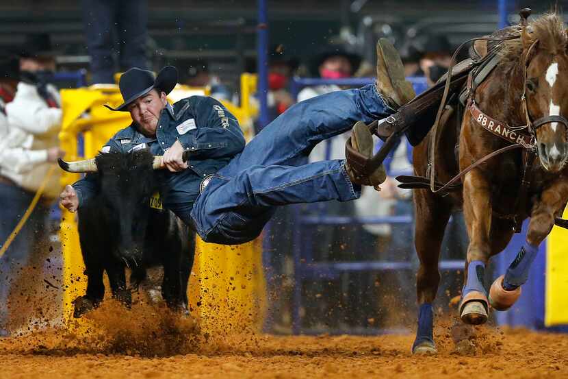 Steer wrestler Jacob Elder slides off his horse and turns a first place time during Round 10...