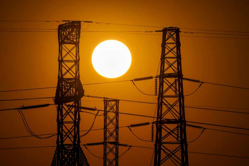 The sun sets behind power lines near Mountain Creek Lake on Monday, July 11, 2022, in Dallas.