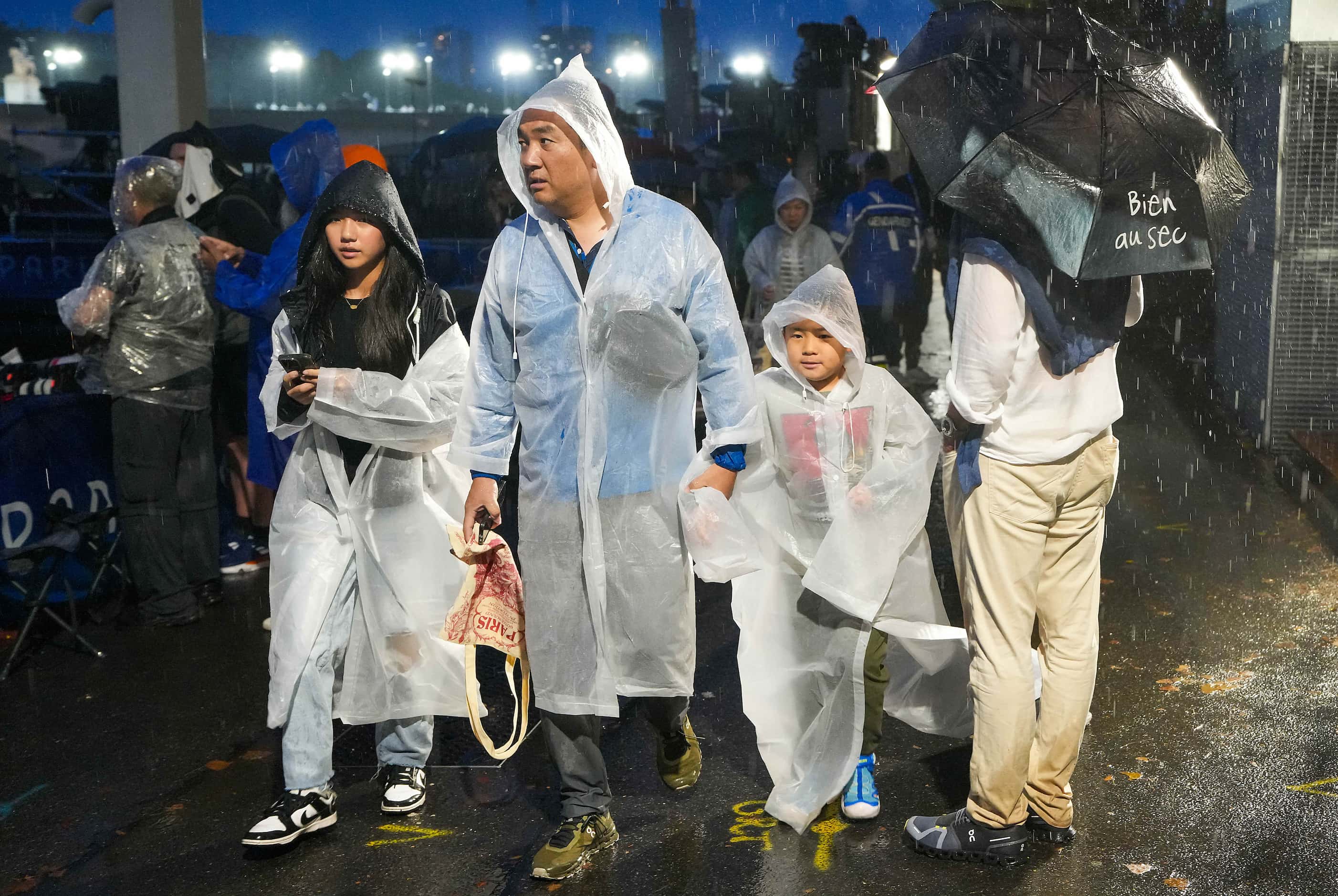 Spectators walk in a heavy rain during opening ceremonies for the 2024 Summer Olympics on...