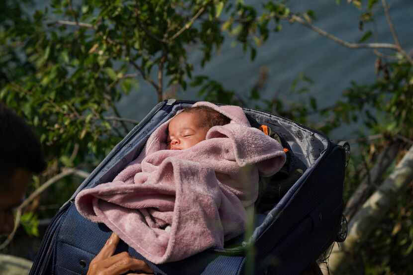 Migrantes cruzan el río Bravo hacia Estados Unidos con un bebé dentro de una maleta abierta,...