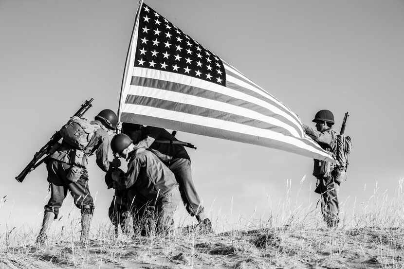A black and white photo of soldiers raising the American flag over a field.