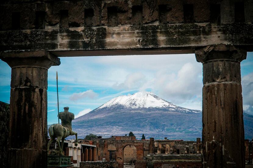 The snow-covered peak of Mount Vesuvius is framed by ancient ruins of the archaeological...