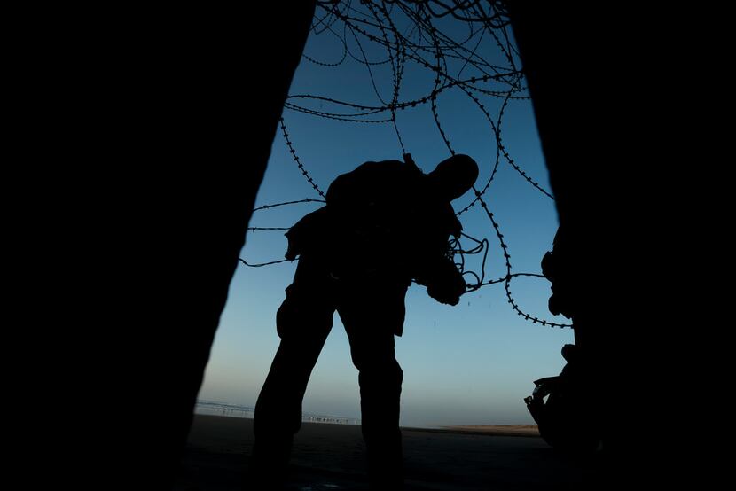 A Border Patrol officer fixes barbed wire at the beach on the U.S. side of the fence between...