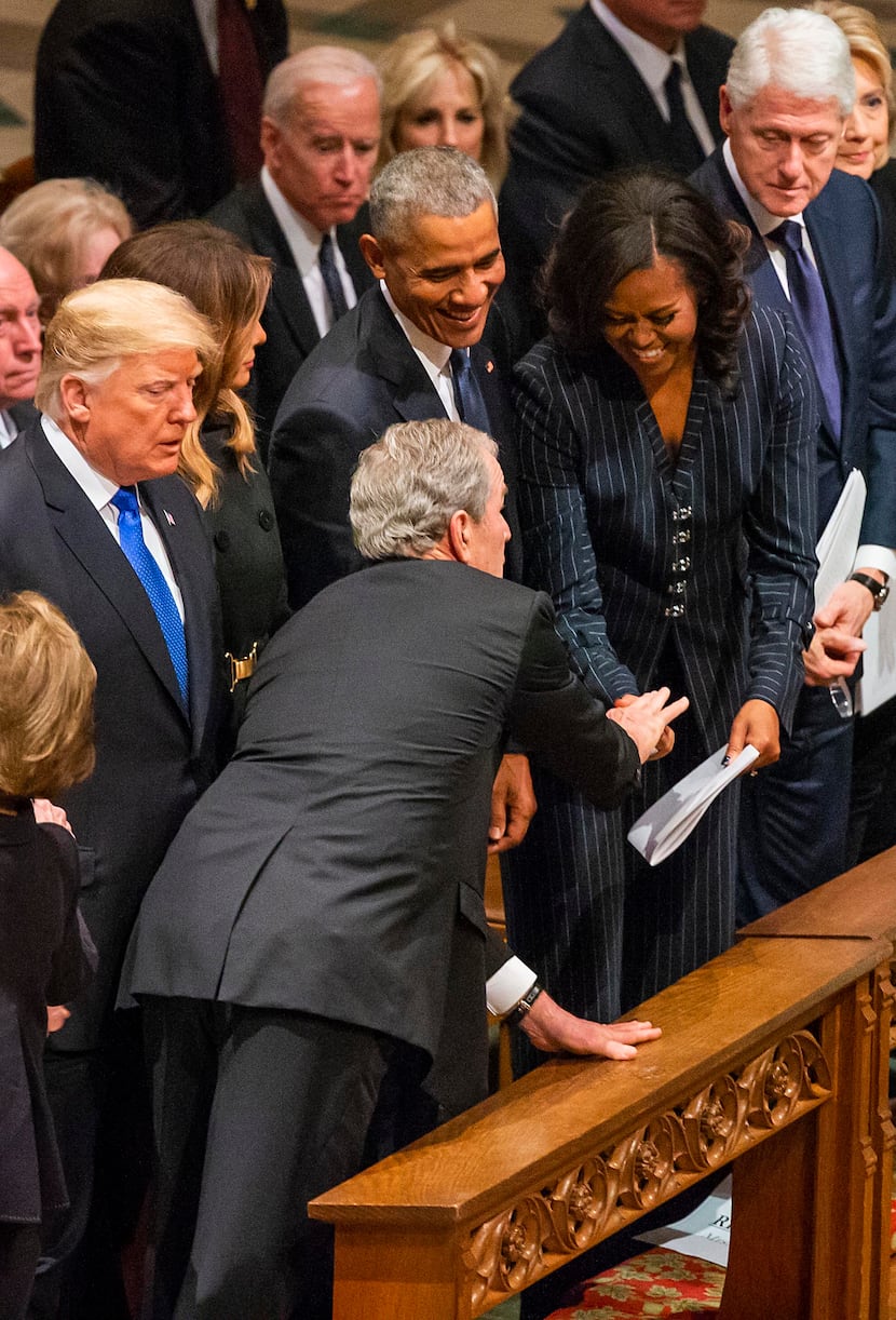 Former President George W. Bush, hands something to a laughing Michelle Obama as (from left)...