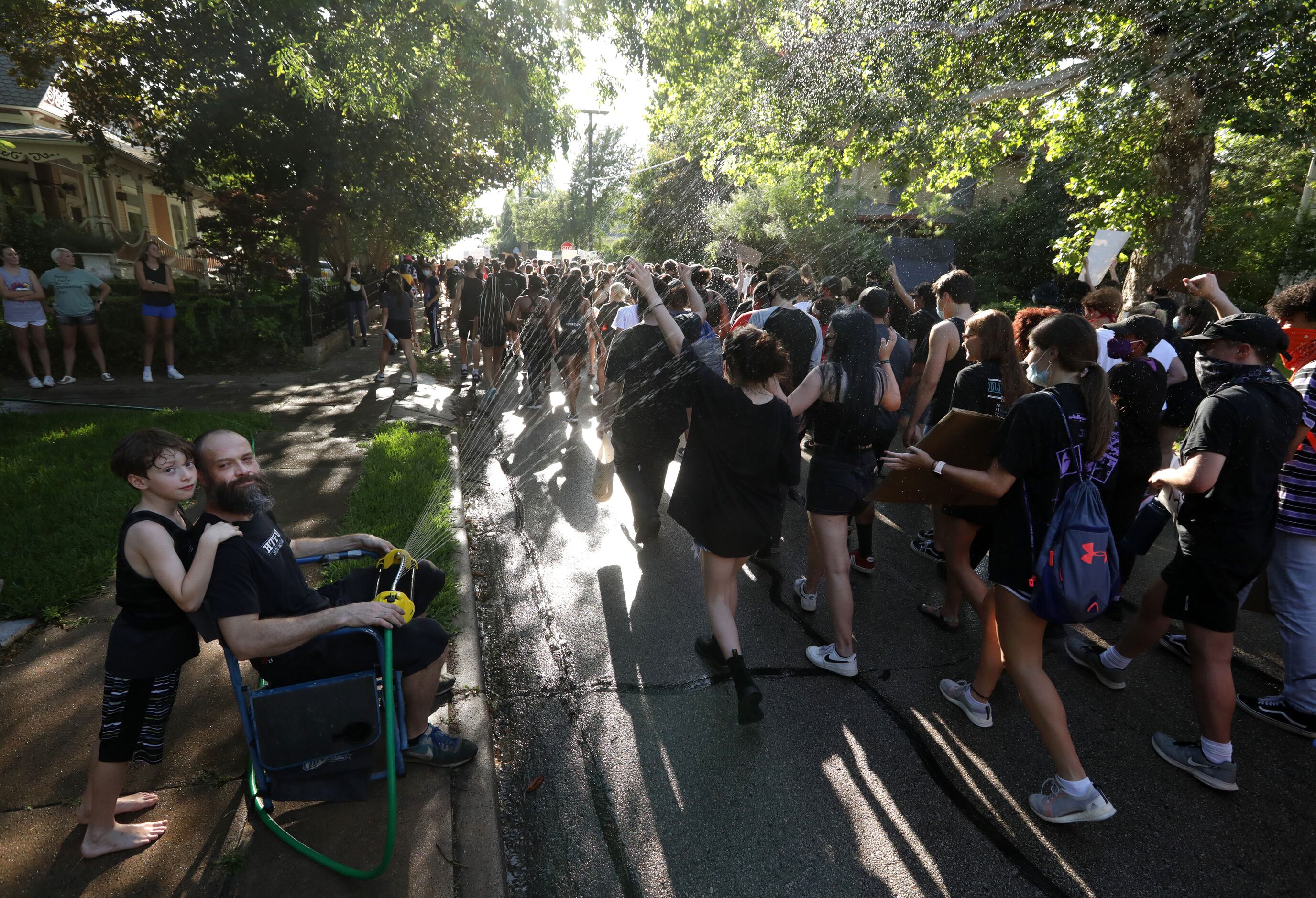 Benjamin Botello, left, helps cool off hot protestors as they march down the streets from...