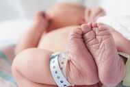 A newborn baby in a hospital bed lying on their back with hospital bracelets on its feet....