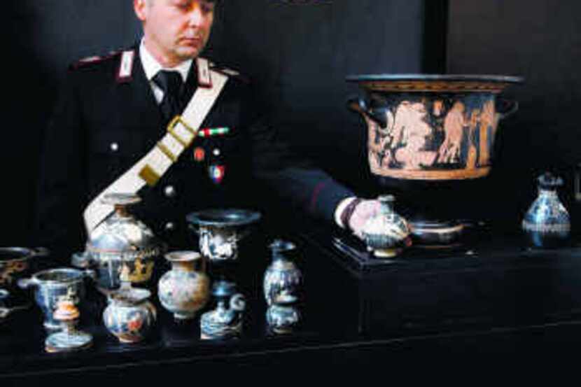 An Italian police officer displays one of the 137 looted artifacts confiscated from a Swiss...