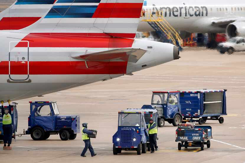 American Airlines crew members move luggage from an aircraft onto carts at Dallas-Fort Worth...