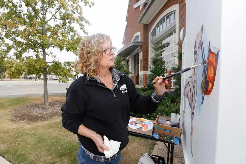 Artist Karen Cox paints a traffic signal box at Fire Station No. 1 in Grand Prairie as a...