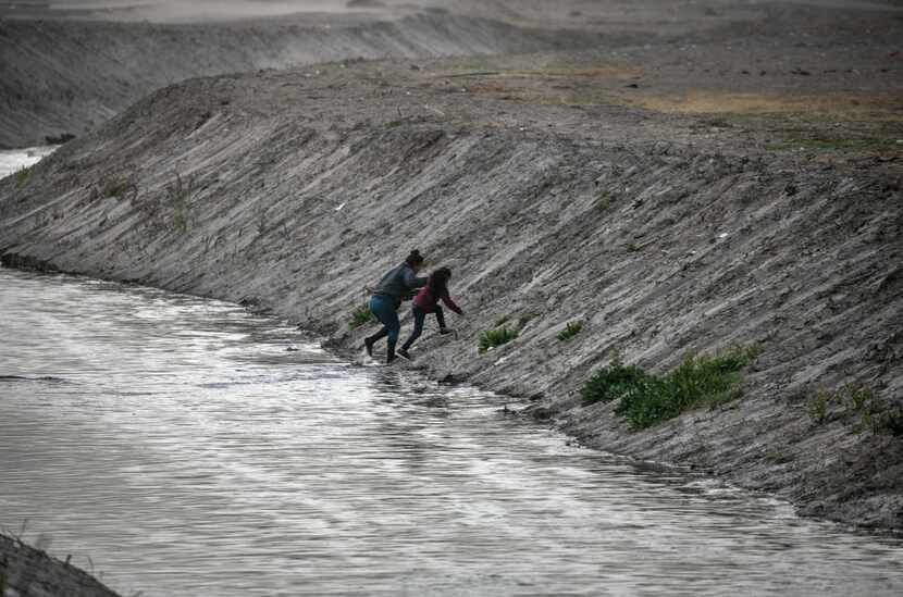 Migrants scramble up the bank of the Rio Grande after crossing from Ciudad Juarez, Mexico,...