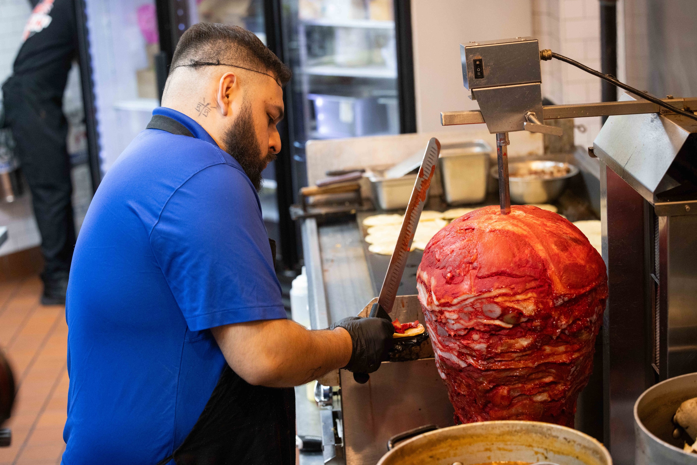 José “Joe” Reyna shaves off the trompo from its rotating spit, a cooking concept inspired by...