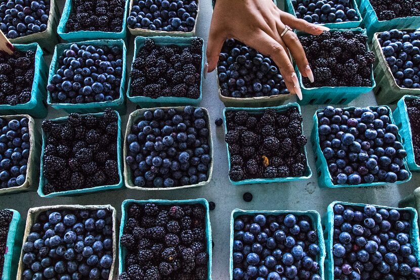 Helen Castillo of Dallas straightens baskets of berries at The Shed at Dallas Farmers Market...