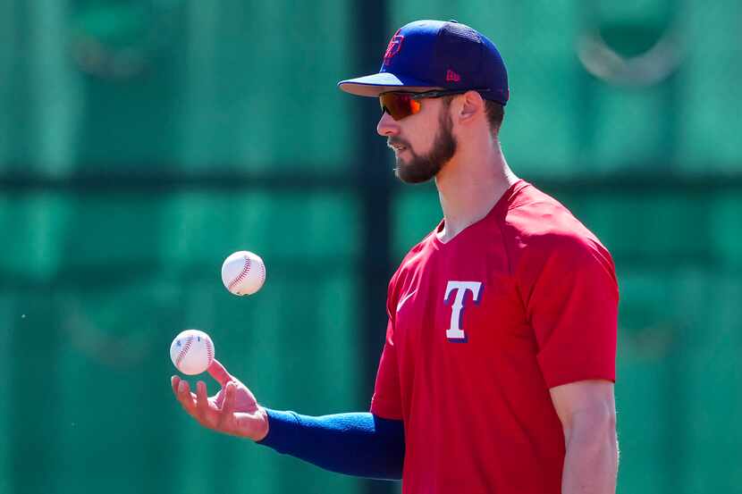 Texas Rangers outfielder Eli White juggles two balls in the outfield during a spring...