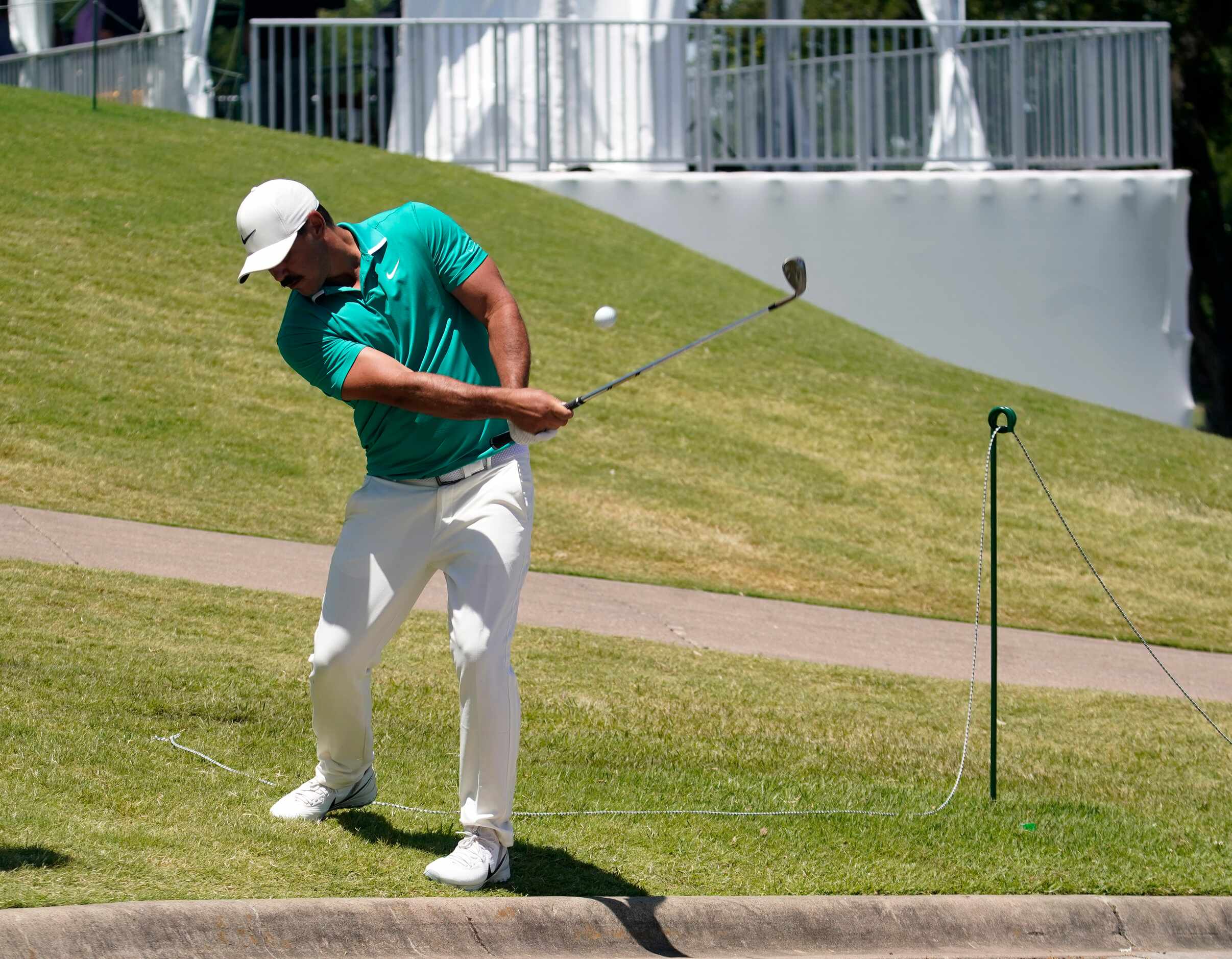 PGA Tour golfer Brooks Koepka chips over a sidewalk after his ball hit the wall behind the...