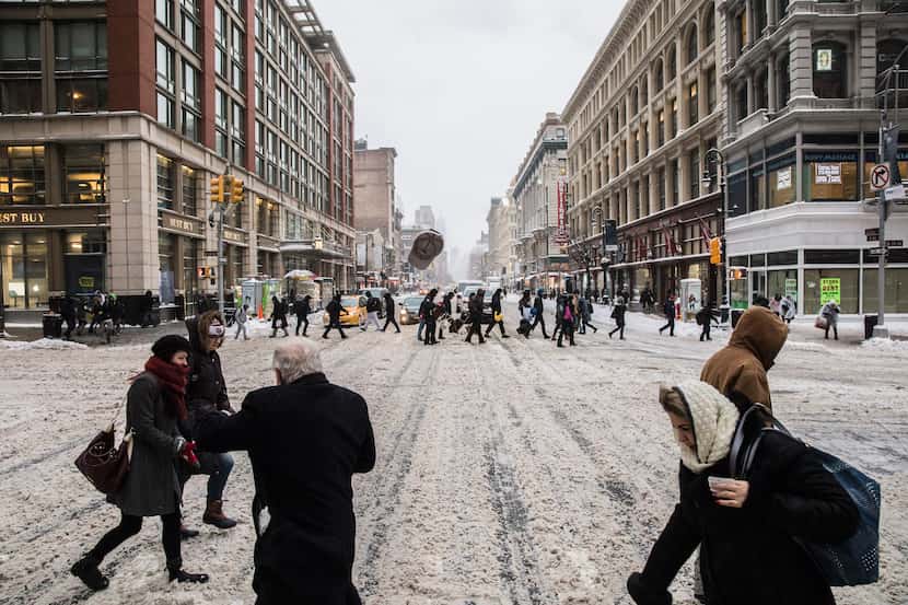 NEW YORK, NY: A man loses his hat as pedestrians cross a snow-covered street in New York,...