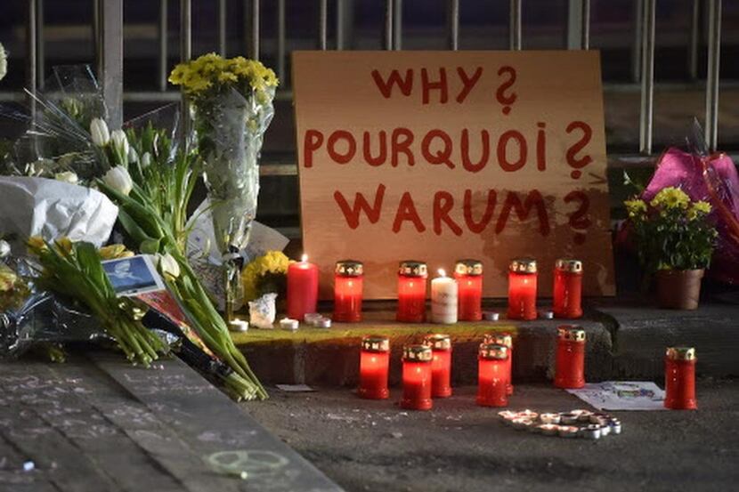 
A sign reads "Why?" in English, French and Flemish behind candles and flowers near the...