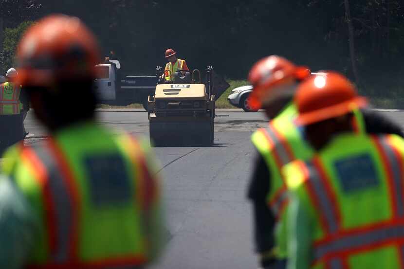 Workers use a steamroller to smooth freshly laid asphalt during a street repaving project. 