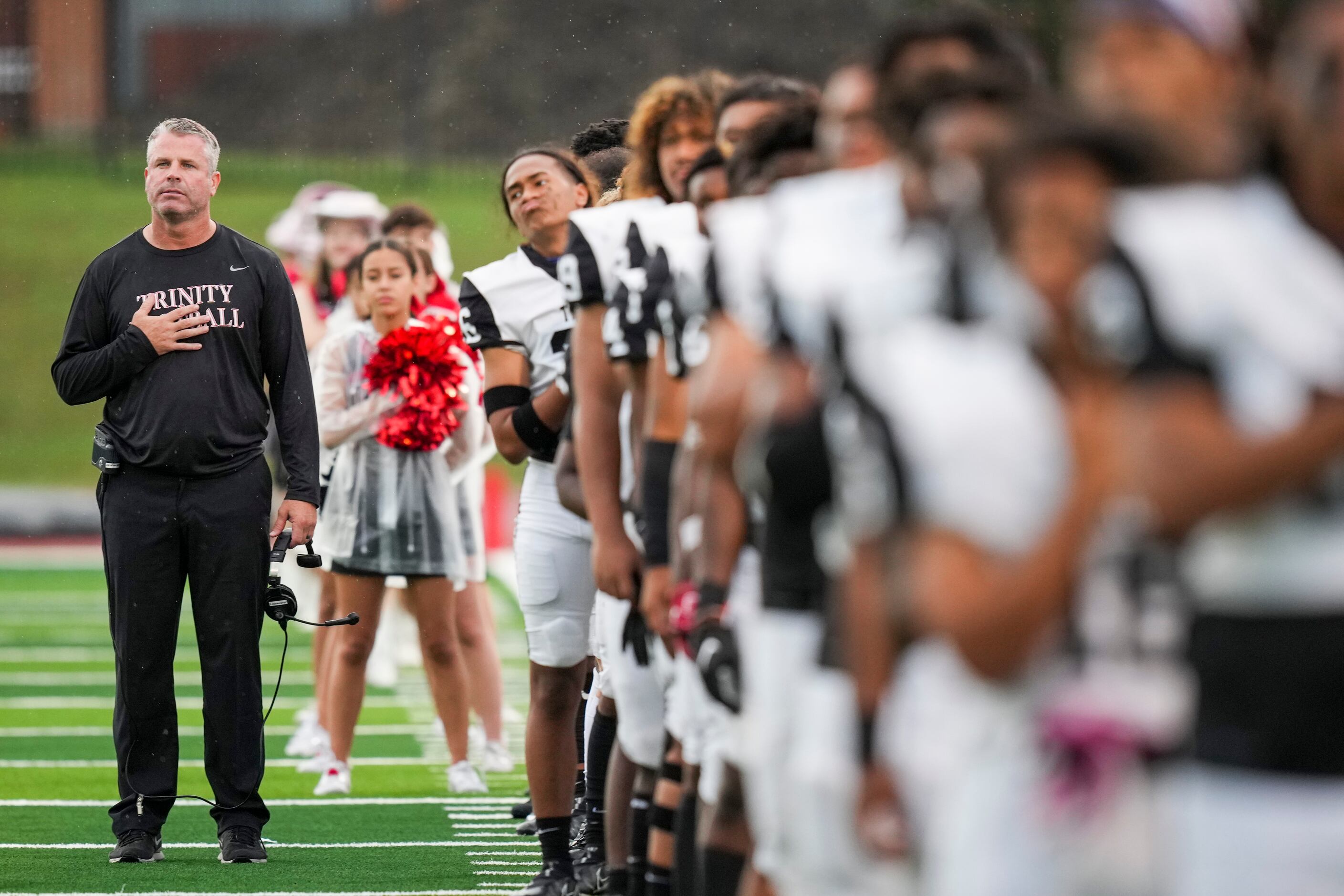 Euless Trinity head coach Aaron Lineweaver stands for the national anthem with his team...