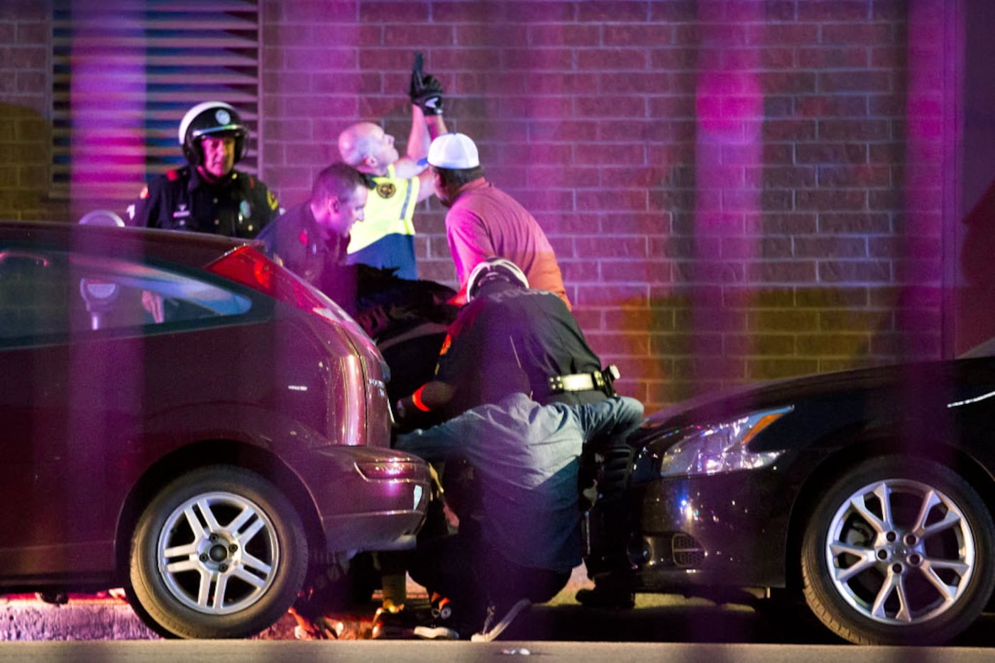 Shetamia Taylor (hunched over, in dark shirt, center) who was shot in the leg, is helped by...