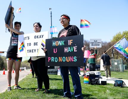 Evren Yurchak, Nadia Haghighatian, and Rosario Sosa hold signs as cars drive by honking...