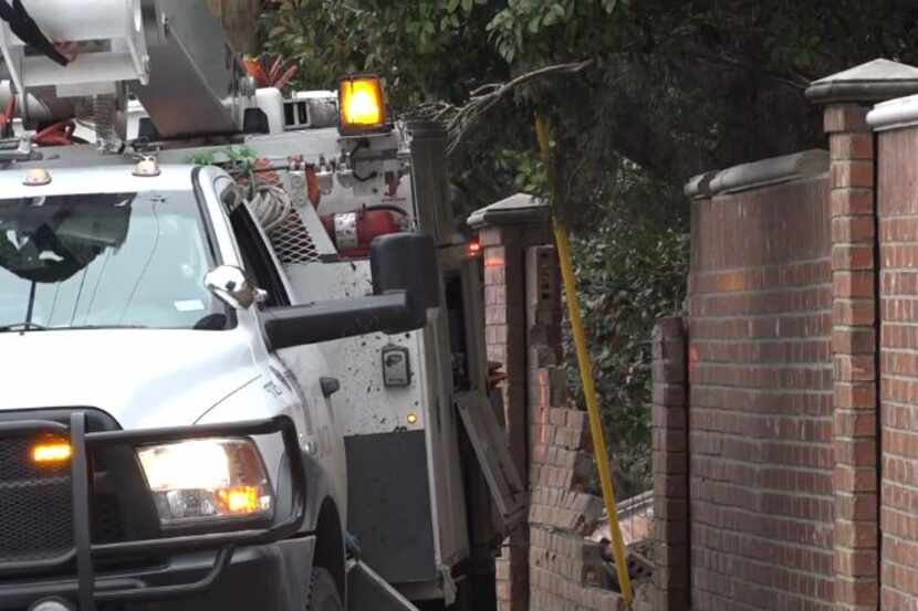 An Oncor repair truck sits next to part of a homeowner's brick wall that was damaged when a...