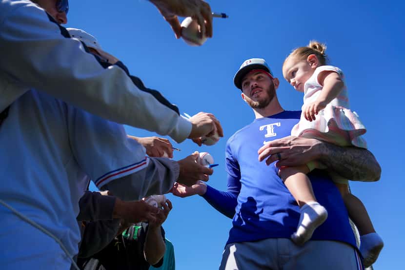 Texas Rangers catcher Jonah Heim stops to sign autographs while holding his daughter Luxx...