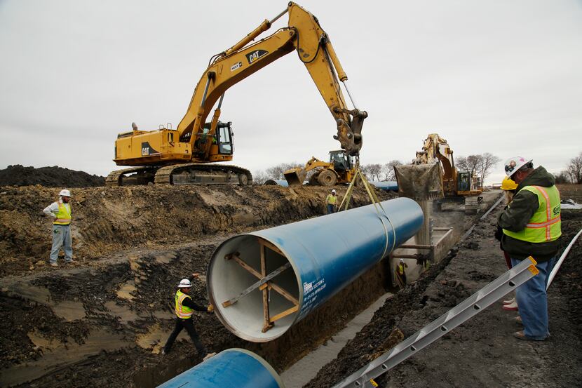 A construction crew installs 50-foot-long sections of pipe near Highway 78 about ten miles...