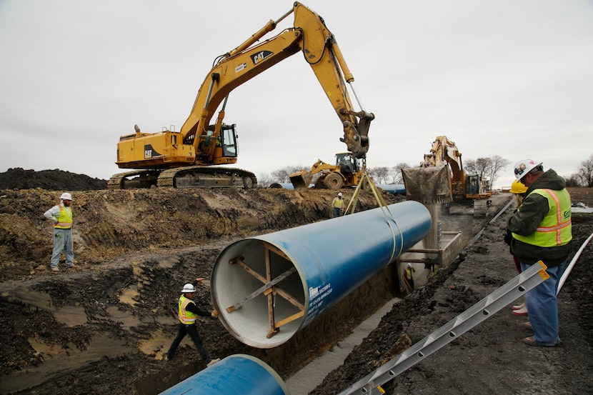 A construction crew installs a 50-foot-long sections of pipe near Highway 78, about 10 miles...