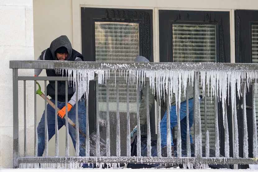 Workers clear debris from a balcony covered in icicles in the Camden Victory Park apartments...