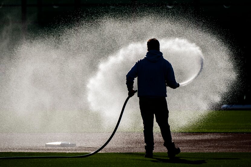 A groundskeeper waters a practice diamond infield at the Texas Rangers' spring training...