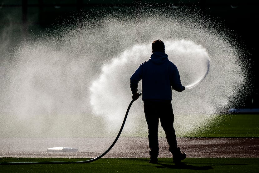 A groundskeeper waters a practice diamond infield at the Texas Rangers' spring training...
