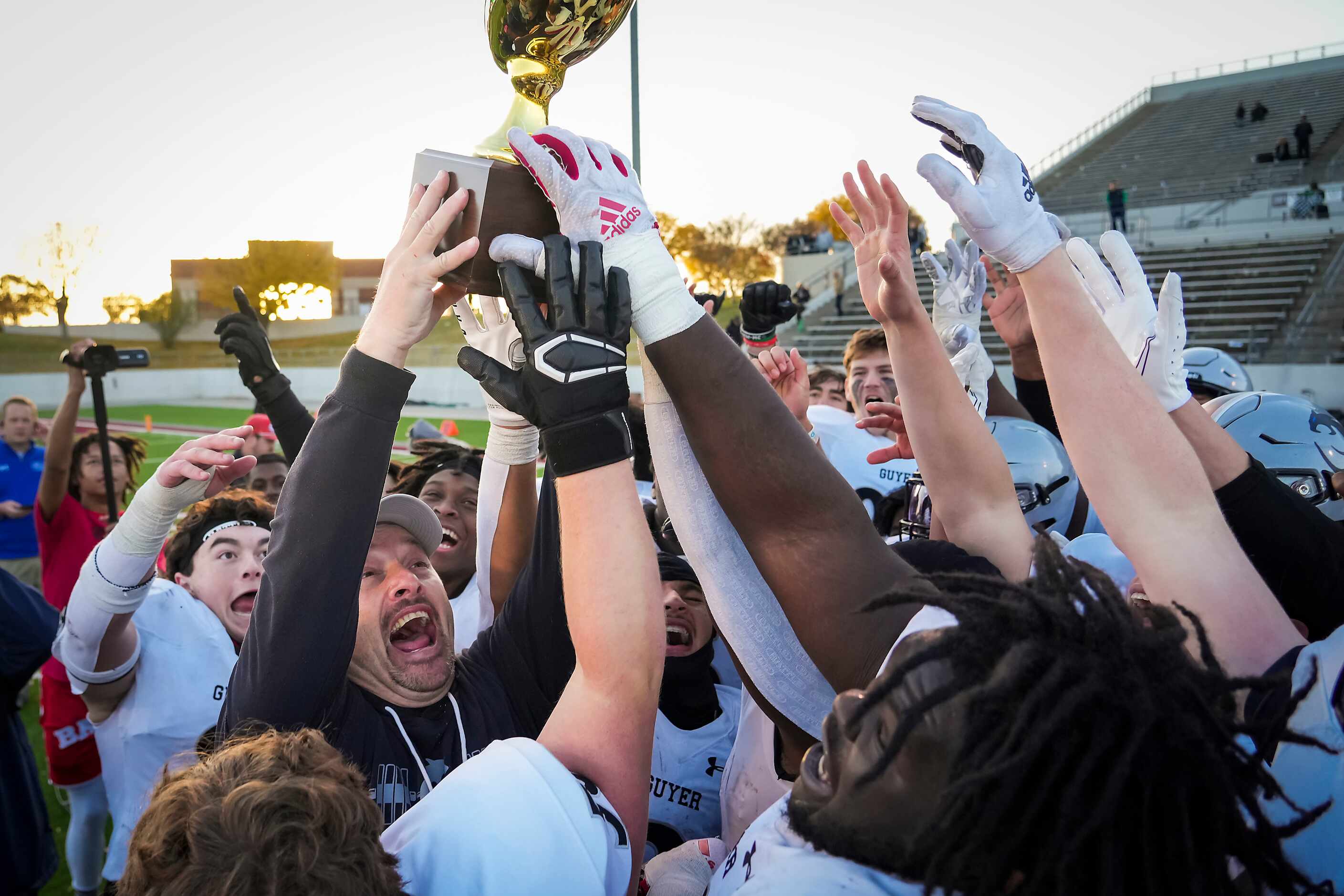 Denton Guyer head coach Reed Heim lifts the game trophy as he celebrates with his players...