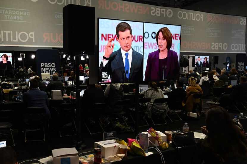 Pete Buttigieg and Amy Klobuchar are shown on screens in the spin room during the debate.