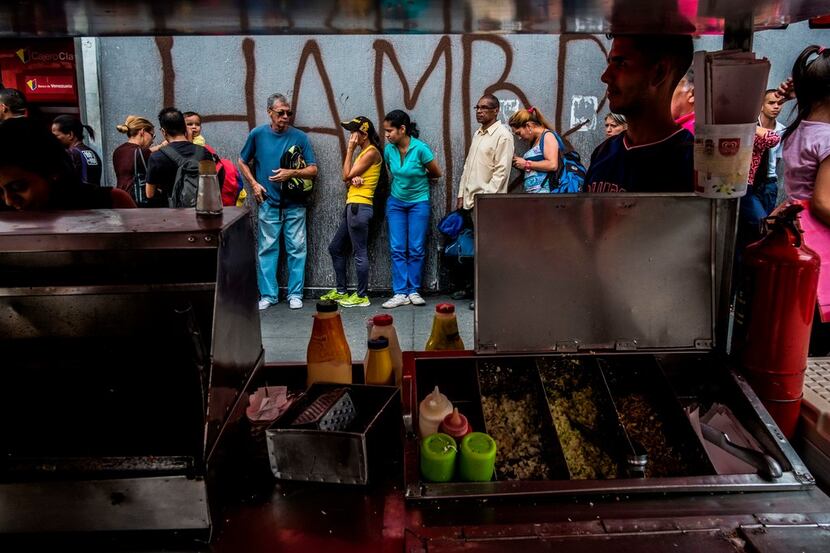 People queue next to a wall with a graffiti reading "Hunger" in Caracas on July 23, 2018....