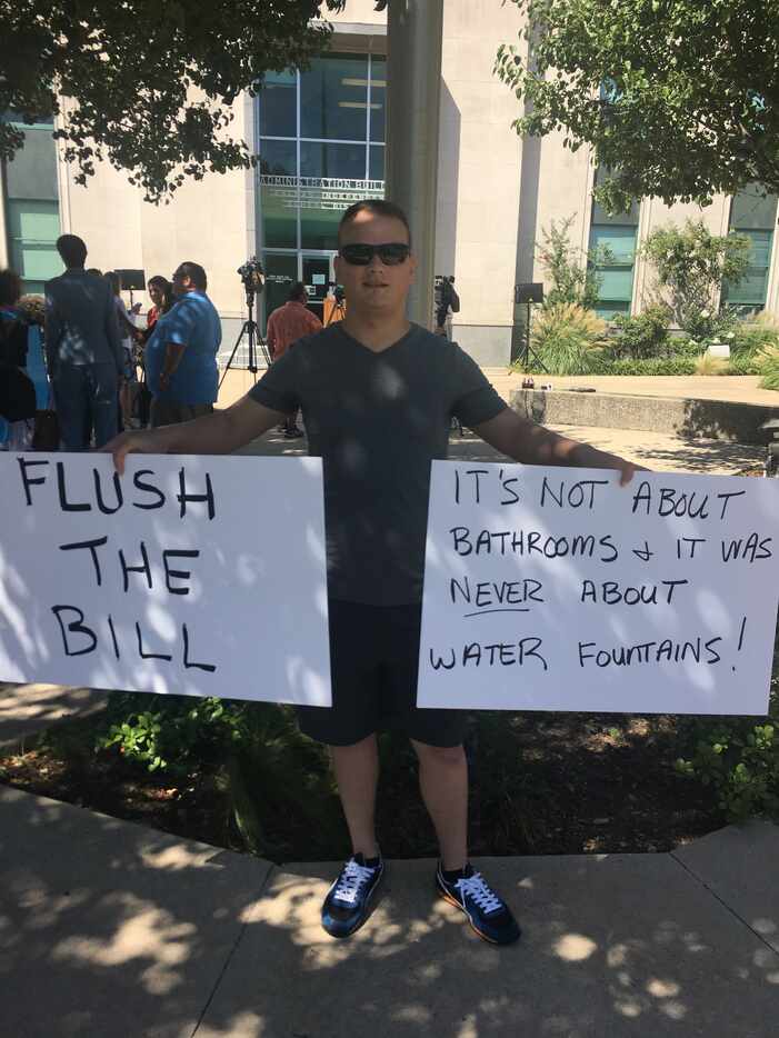 Justin Culpepper holds two signs at a demonstration against Texas' so-called bathroom bill.
