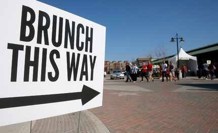 People walk by a sign during Morning After Brunch Festival at Dallas Farmers Market in...