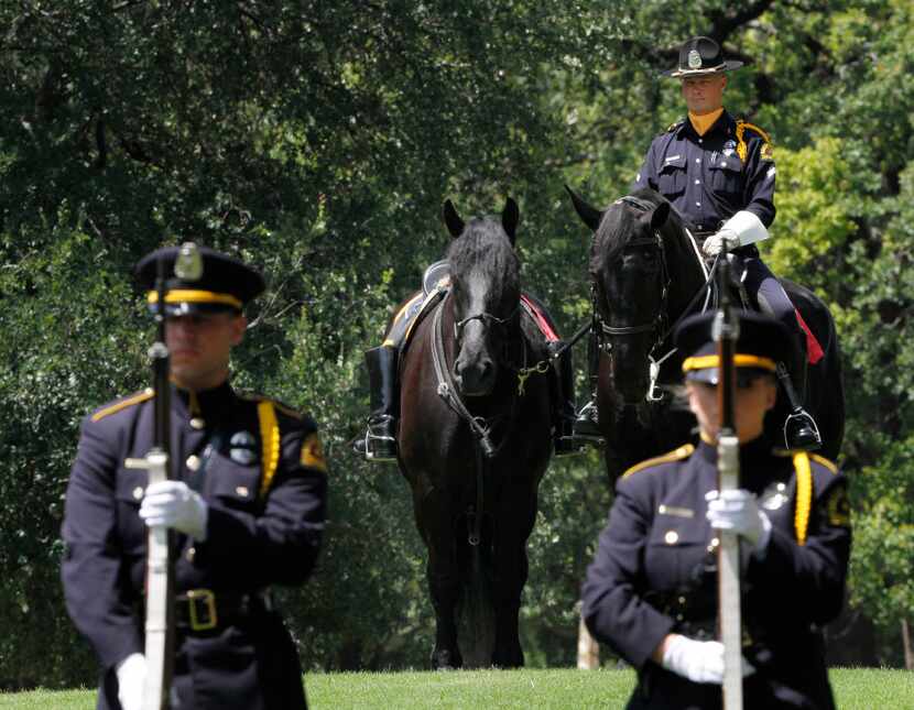 Dallas Police officer Ron Cunningham sits with a riderless horse as 21 Gun Salute officers...
