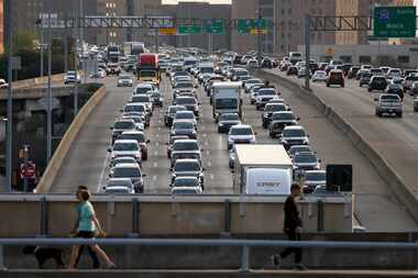 Traffic crawls along Woodall Rodgers Freeway in Dallas as pedestrians cross over the freeway...