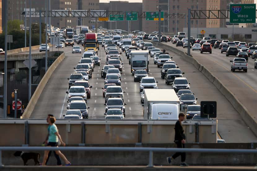 Traffic crawls along Woodall Rodgers Freeway in Dallas as pedestrians cross over the freeway...